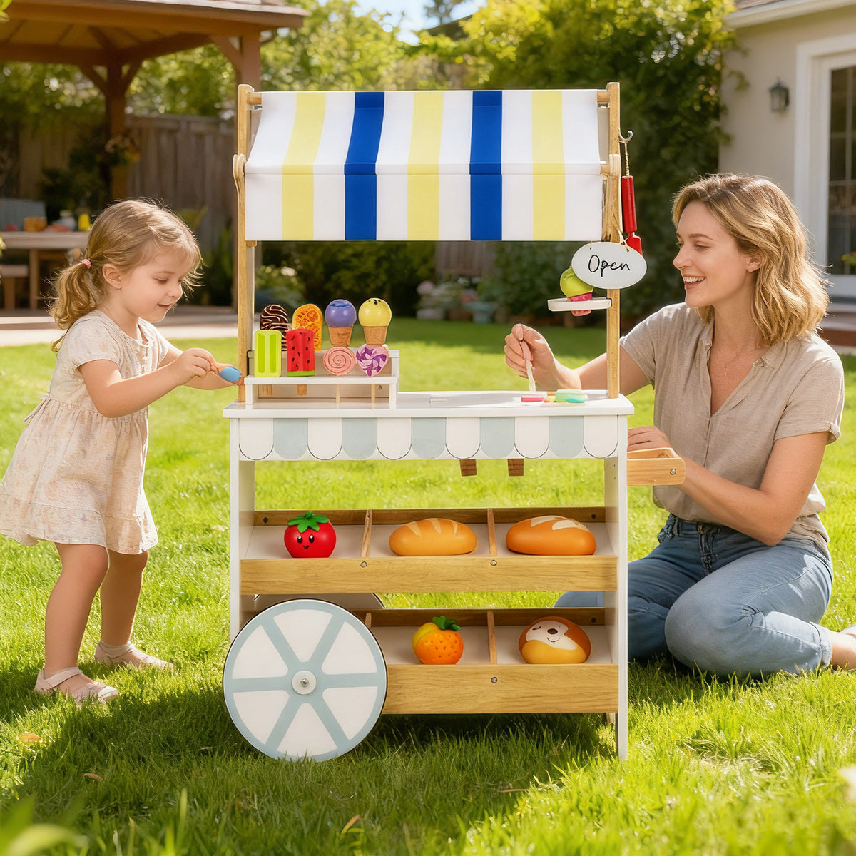 A mother and daughter play with the wooden ice cream cart in the garden
