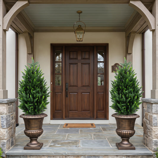 2 Pack 90 CM Artificial Cypress Topiary Trees, the faux plants placed in large bronze urns on either side of a wooden front