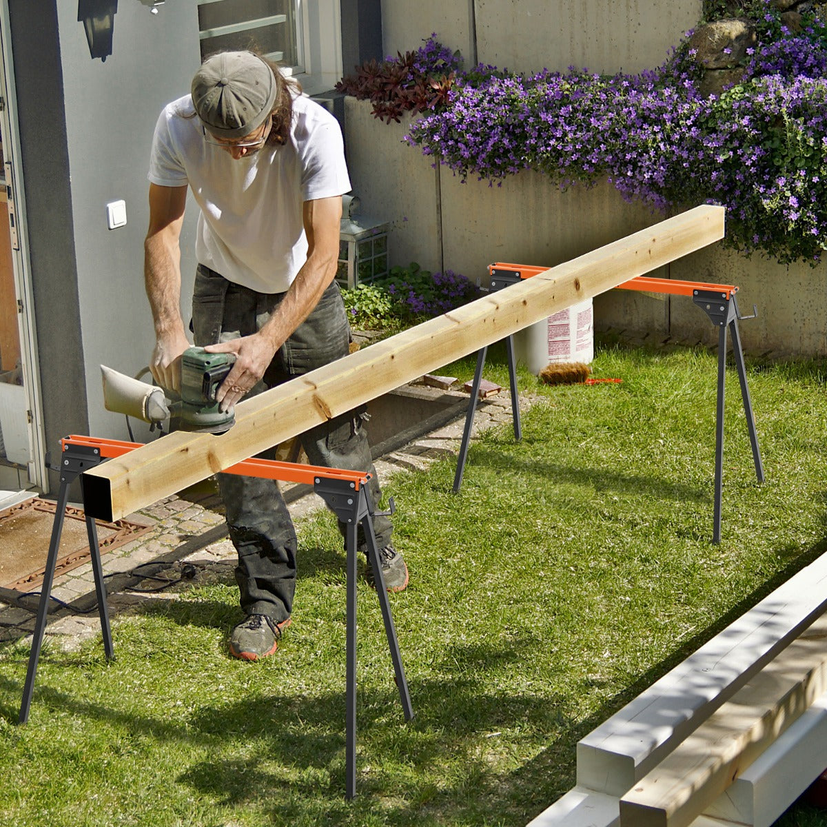 Man sanding a wooden beam supported by two orange and black portable saw horse work tables in a garden