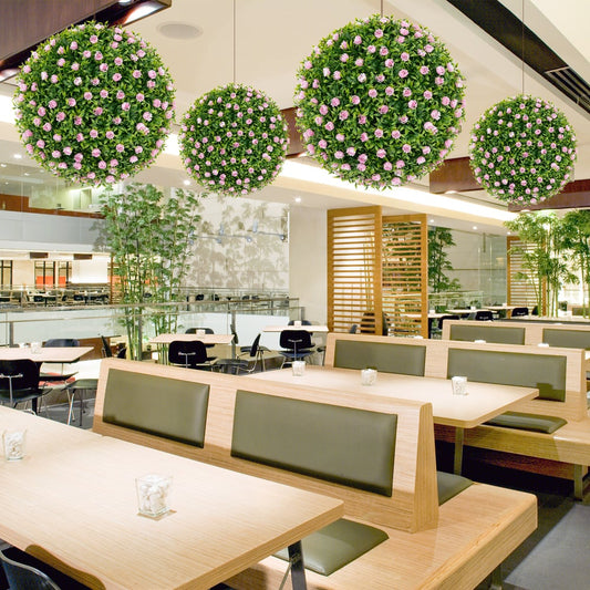 These artificial plant topiary balls with pink flowers are displayed hanging in a restaurant setting