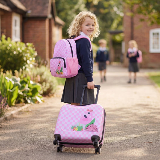 A young girl smiles pulling a pink and white kids luggage set with a matching backpack on a path