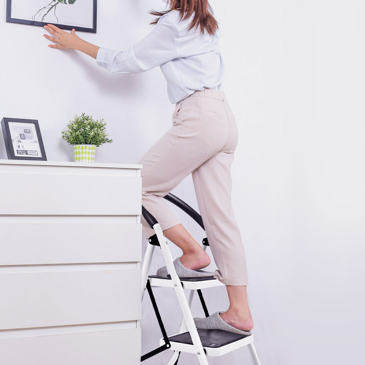 The household ladder with anti-slip platform, a woman hangs a picture