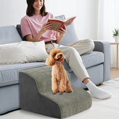 The pet stairs positioned next to a sofa where a person is reading a book with a dog