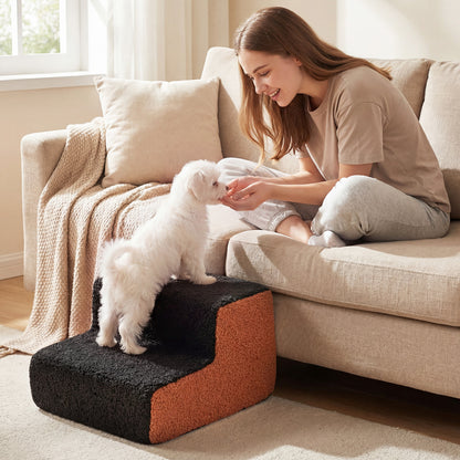 A woman on a sofa offering a treat to a small dog on the pet stairs