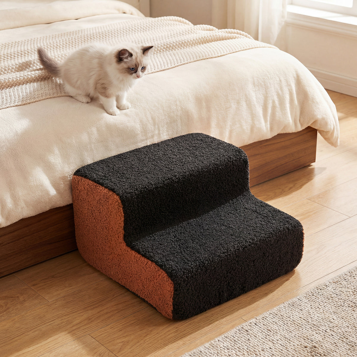 A kitten walking on the pet stairs next to a bed