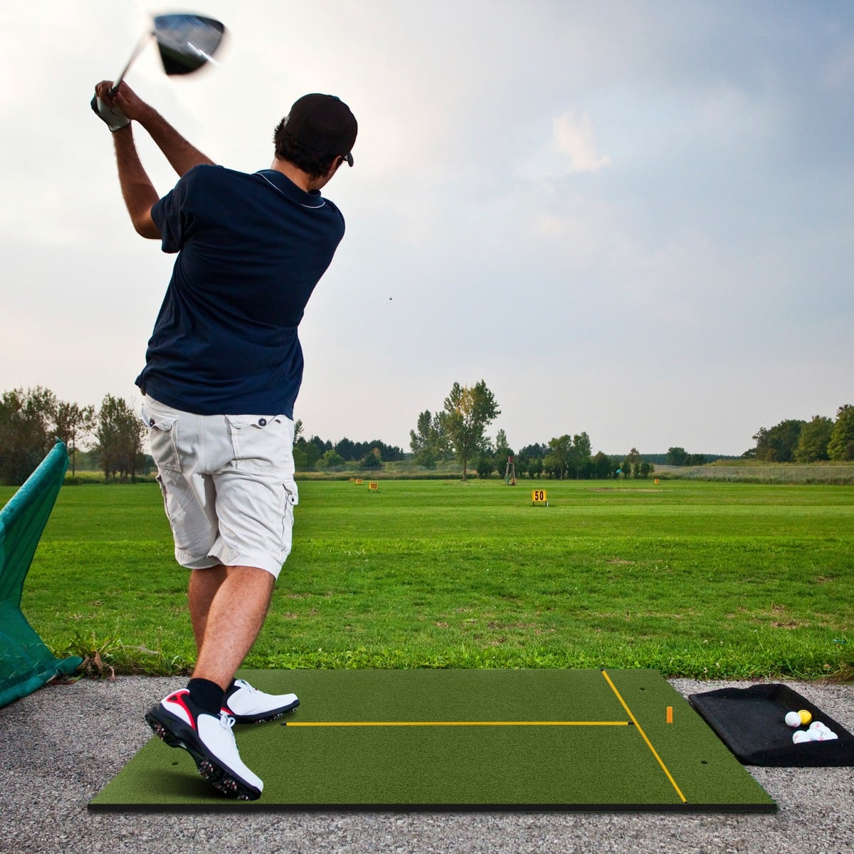 Man swinging a golf club on a golf hitting mat outdoors