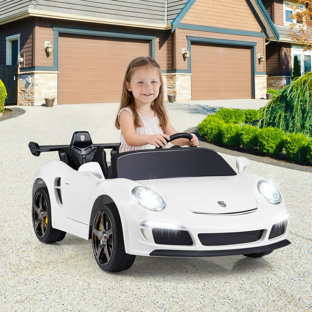 A young girl happily drives the white kids electric car on a paved driveway