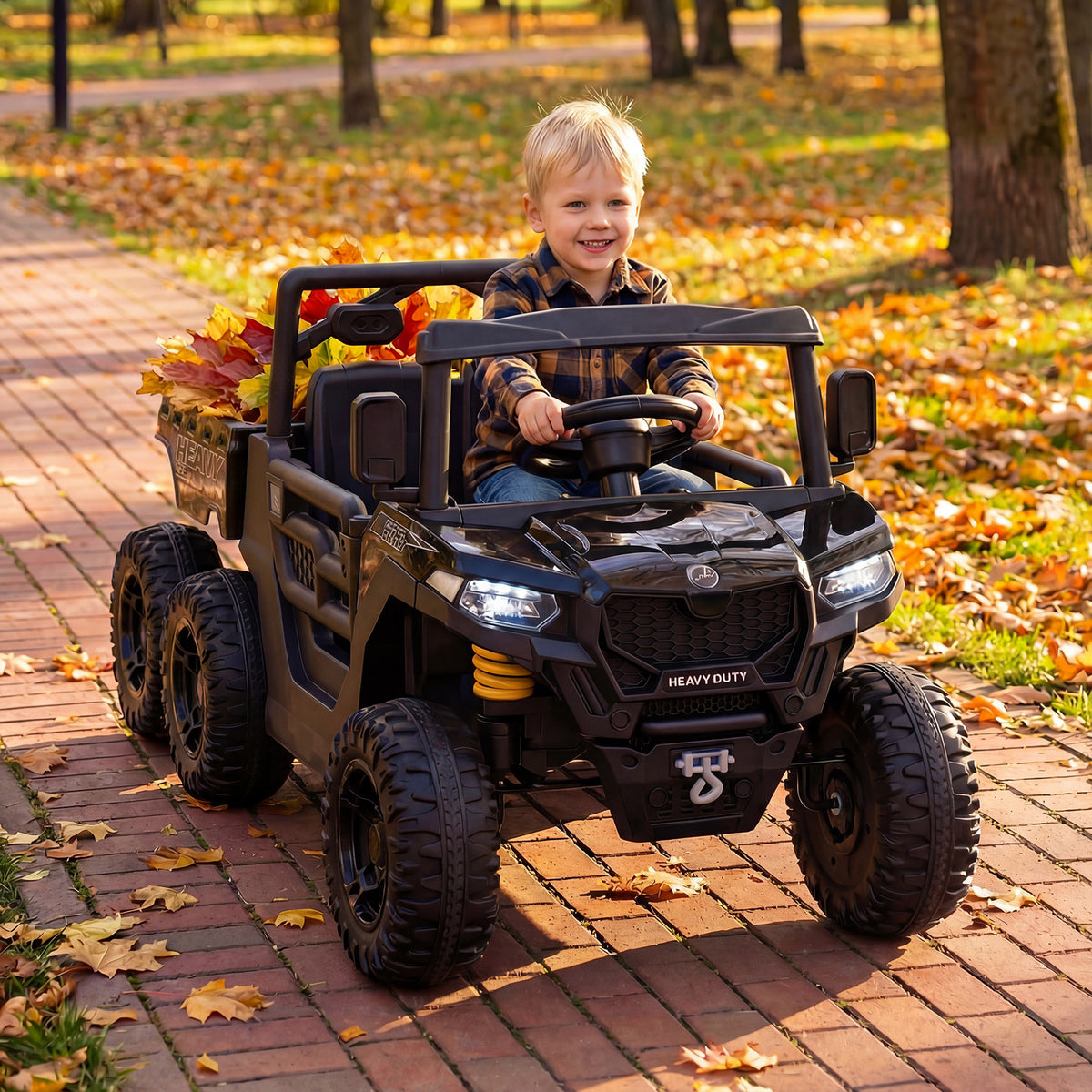Child driving the black electric dump truck in a park with autumn leaves