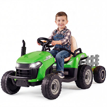 A young boy sits on the green ride on tractor with trailer, smiling at the camera
