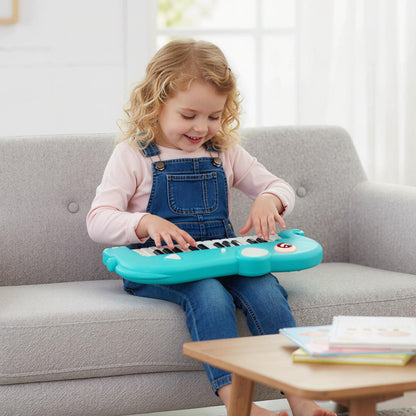 A young child sits on a sofa playing the blue elephant piano keyboard