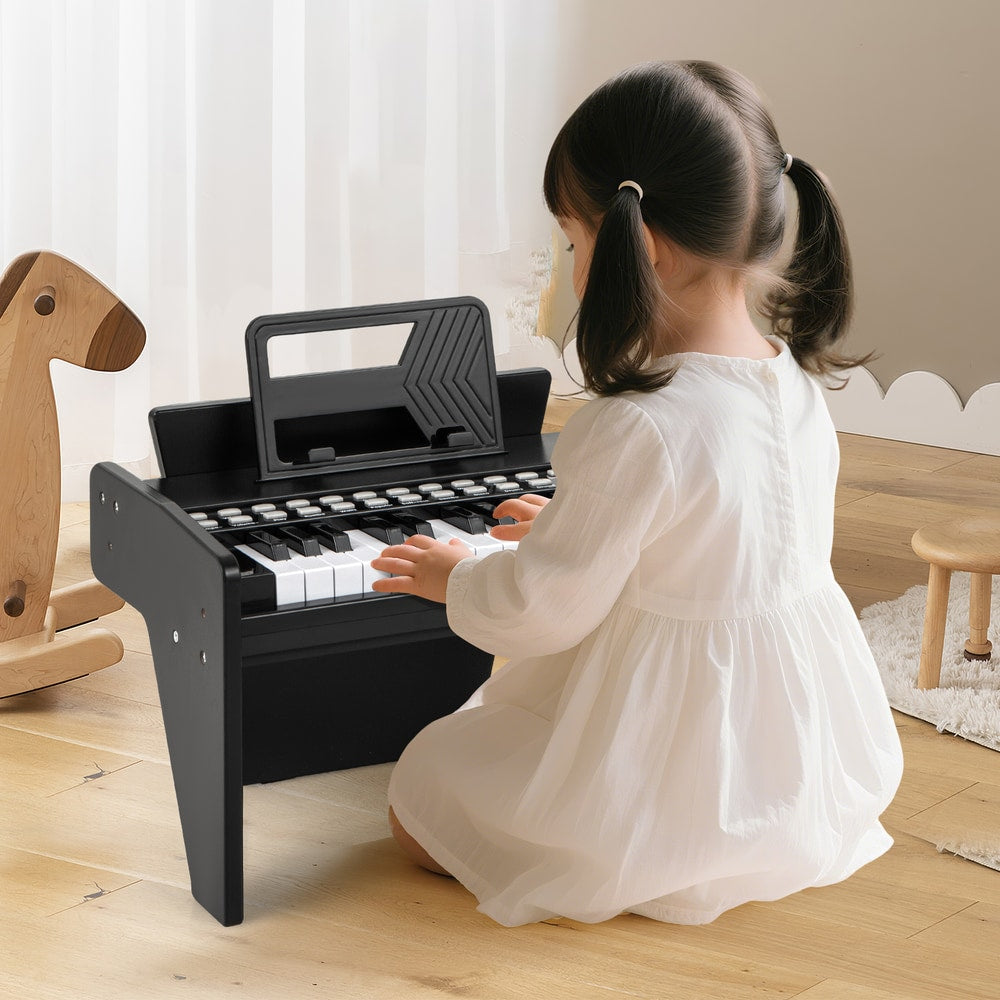 A young girl in a white dress playing the black wooden toy piano