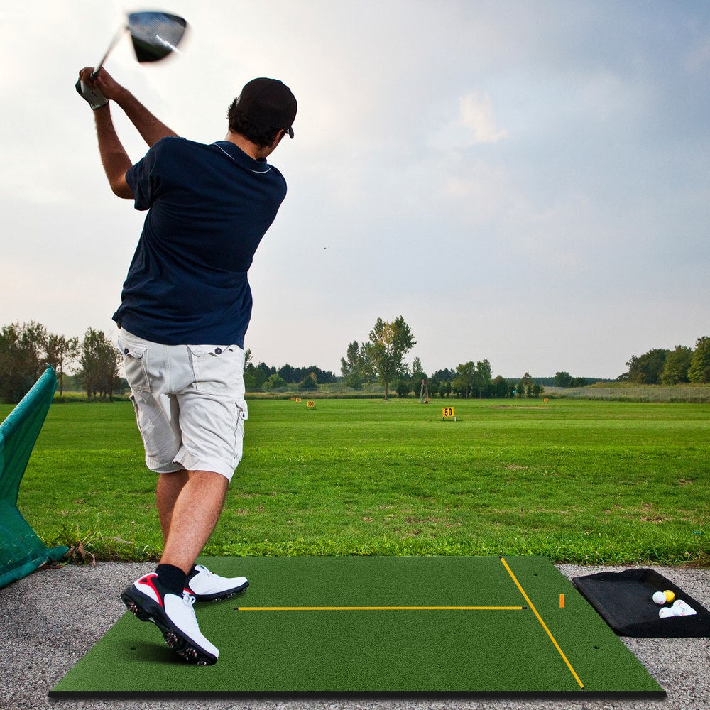 Golfer swinging a club on the golf hitting mat outdoors on a sunny day