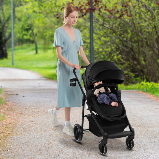 A woman pushing the black baby stroller with a child sitting inside on a paved path outdoors