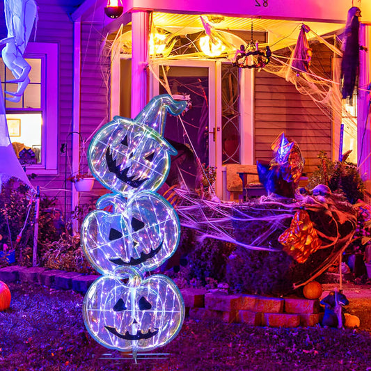 Stacked pumpkin Halloween decoration lit up and placed on a lawn at night with spooky decorations