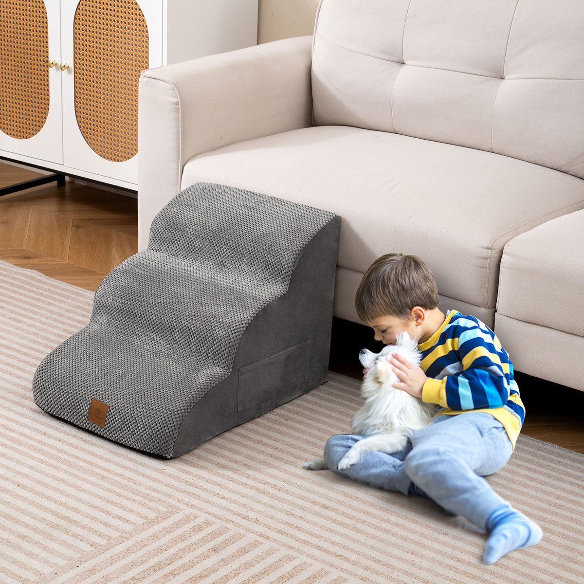 A child sits on the floor next to a grey foam dog ramp, petting a small dog