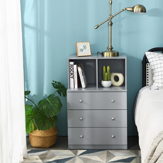 Grey three-drawer dresser with open compartments placed next to a bed in a bedroom setting