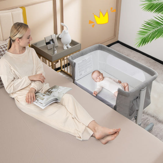 A baby sleeps peacefully in the bedside sleeper next to a woman sitting on a bed