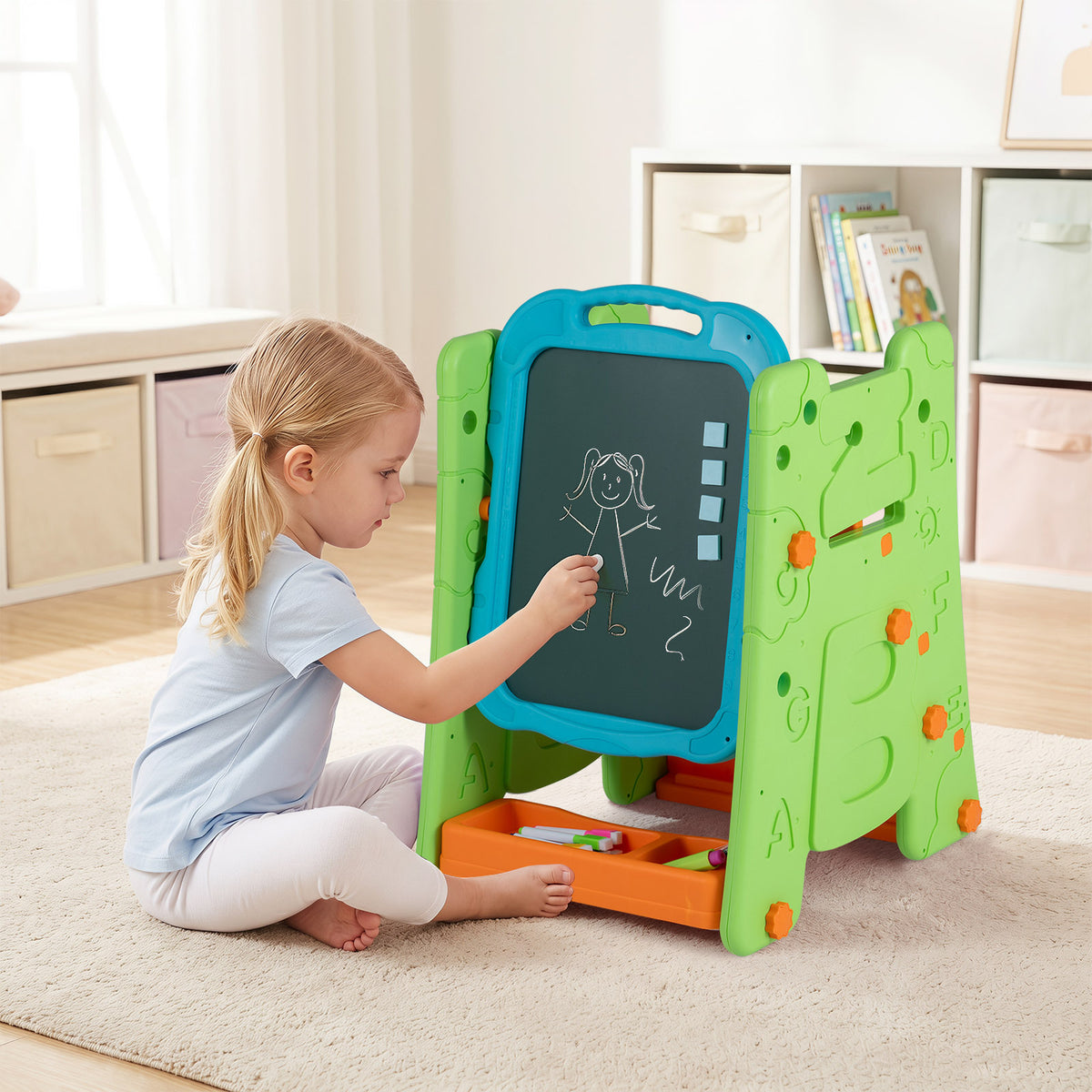 A young girl sitting on a rug drawing on the chalkboard side of the art easel