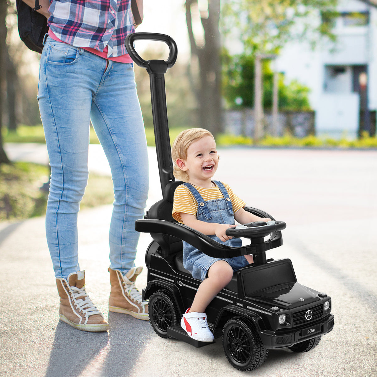 Woman pushing a baby in the black sliding walker with push handle on a pavement