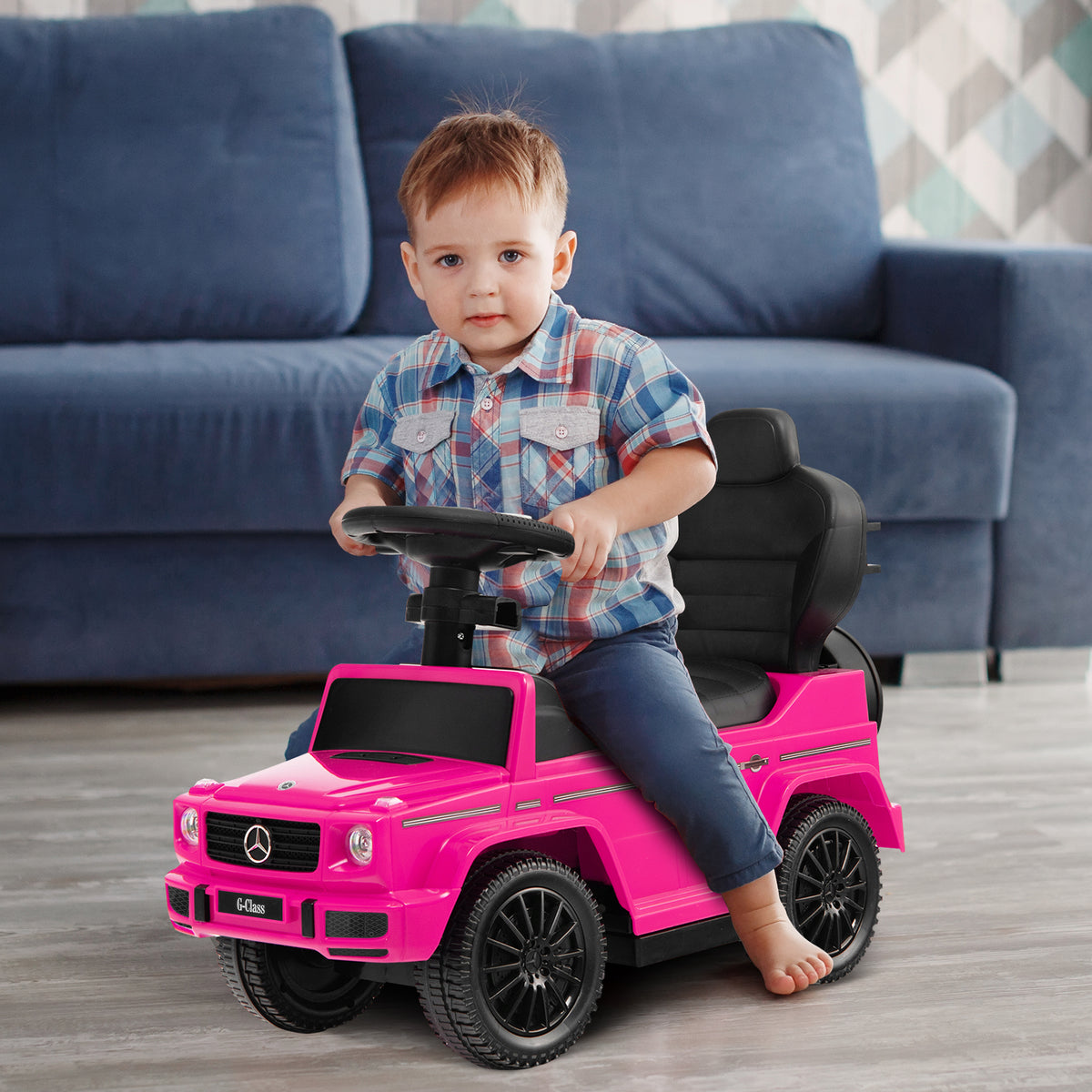 A toddler boy sits at the steering wheel of the pink baby sliding walker
