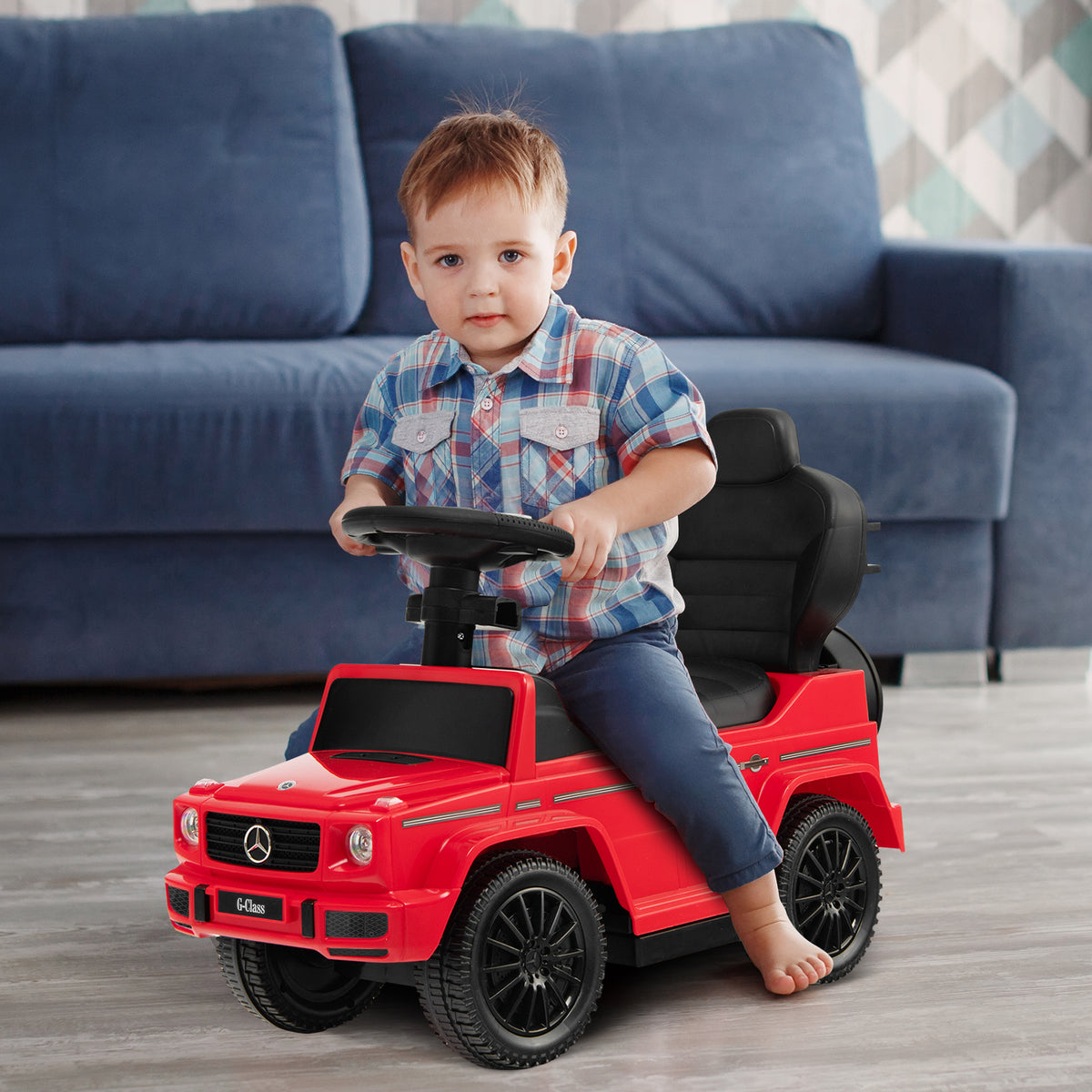 A young boy sits in the red baby walker steering it indoors