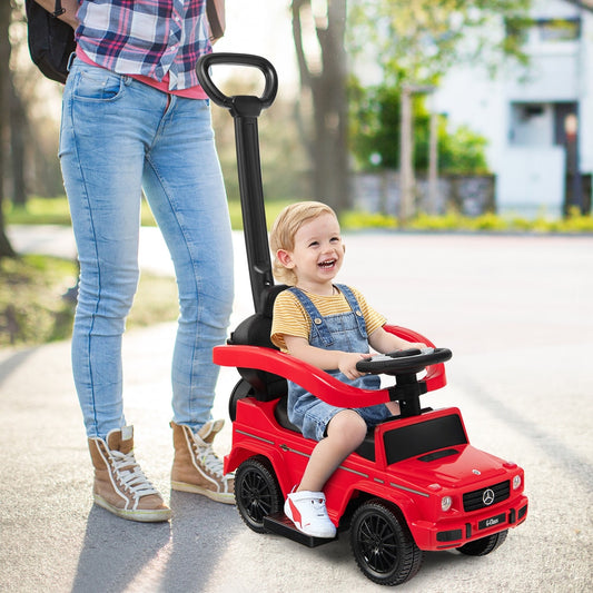 The red baby walker with a push handle being steered by a smiling toddler outdoors