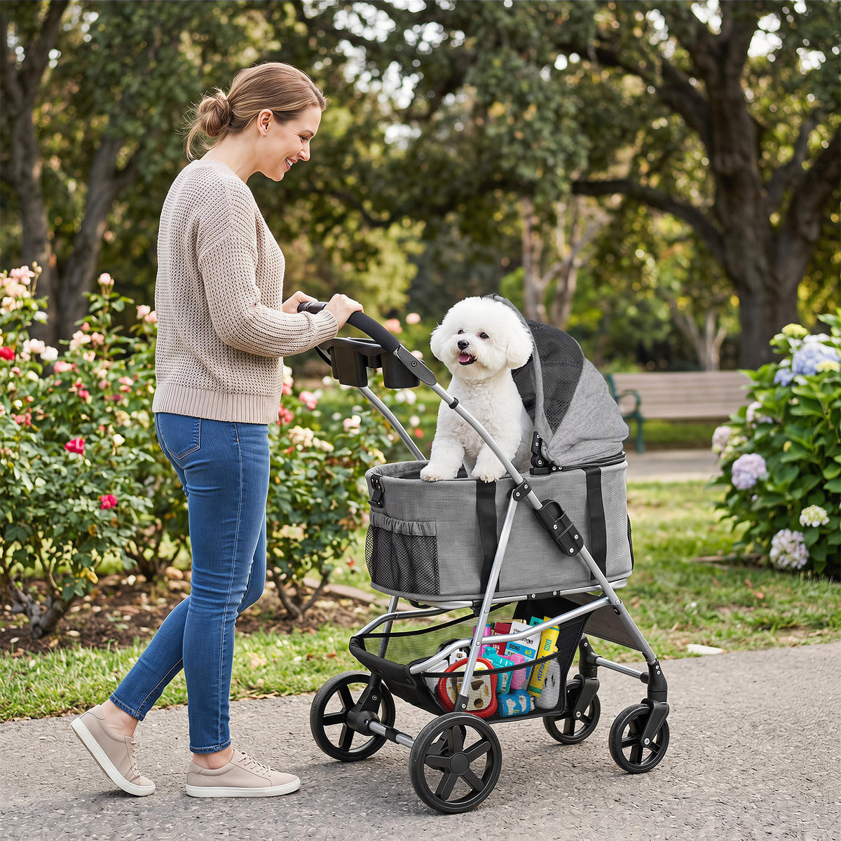 A woman pushes a white bichon frise dog in a grey dog stroller along a path