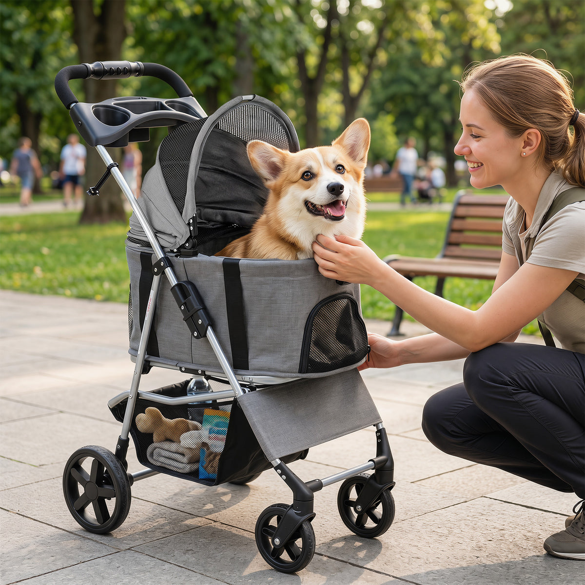 A woman smiles at a corgi dog in the grey dog stroller while walking in a park