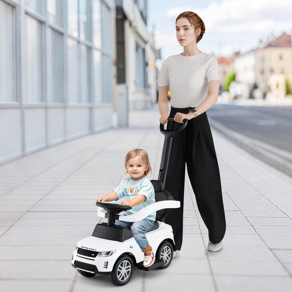 A woman pushes a toddler in the white ride on toy along a pavement