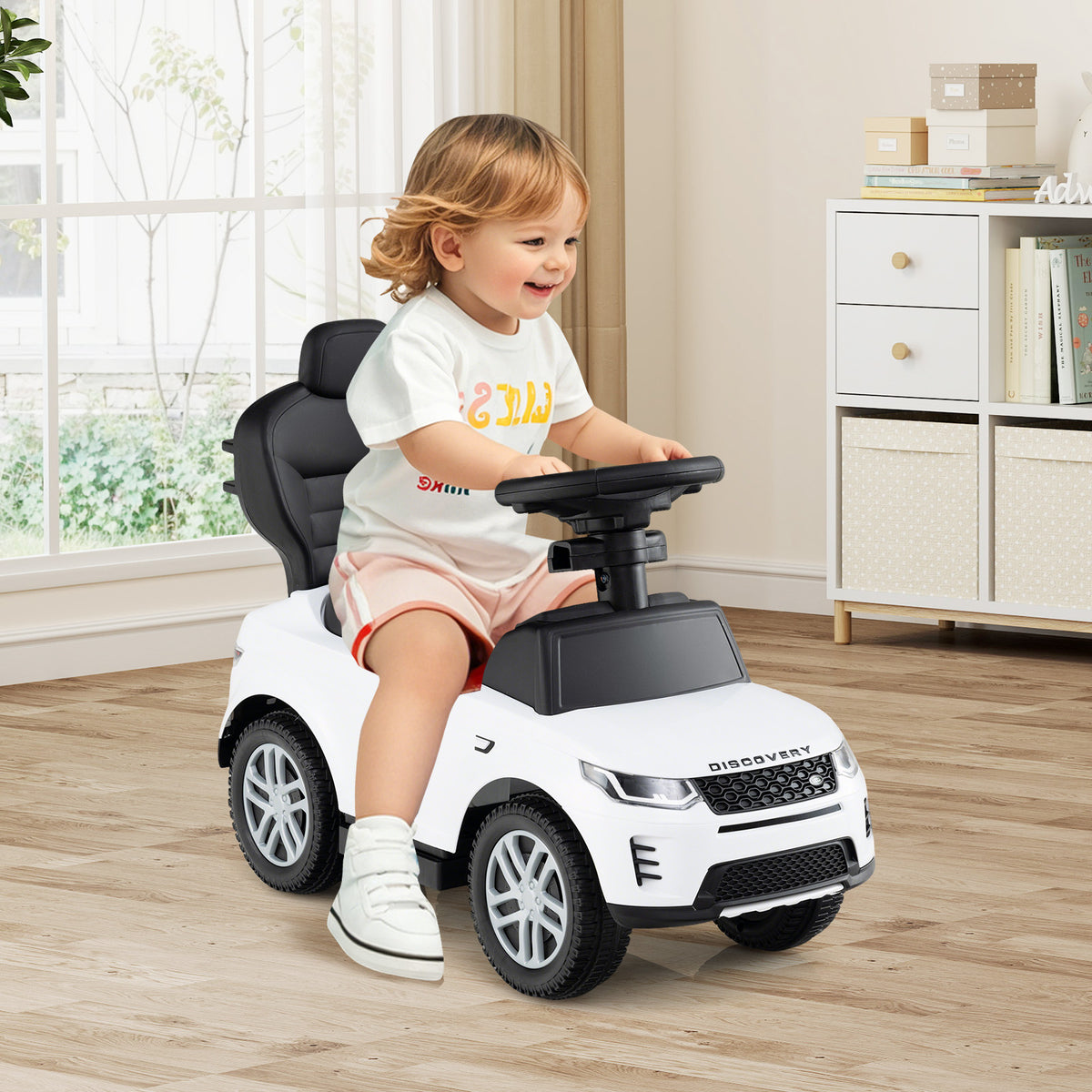 A toddler sits in the white ride on toy, steering and smiling