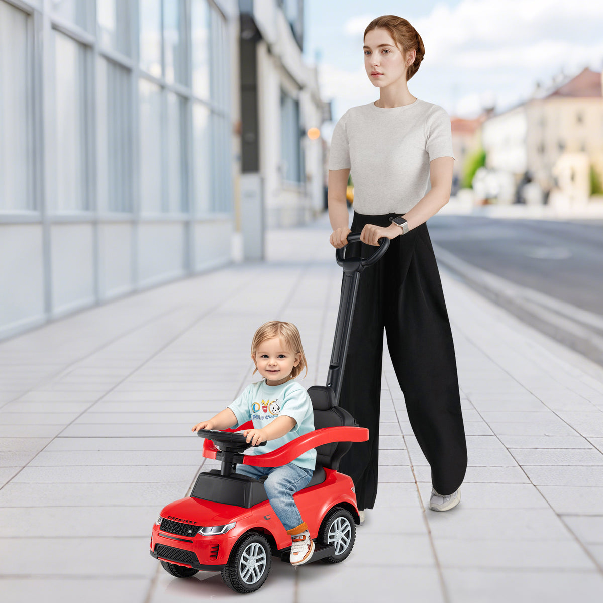 Woman pushing a toddler on the red ride on toy car on a pavement