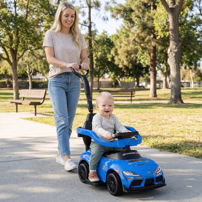 A smiling baby rides in a blue push car while a woman pushes from behind in a park