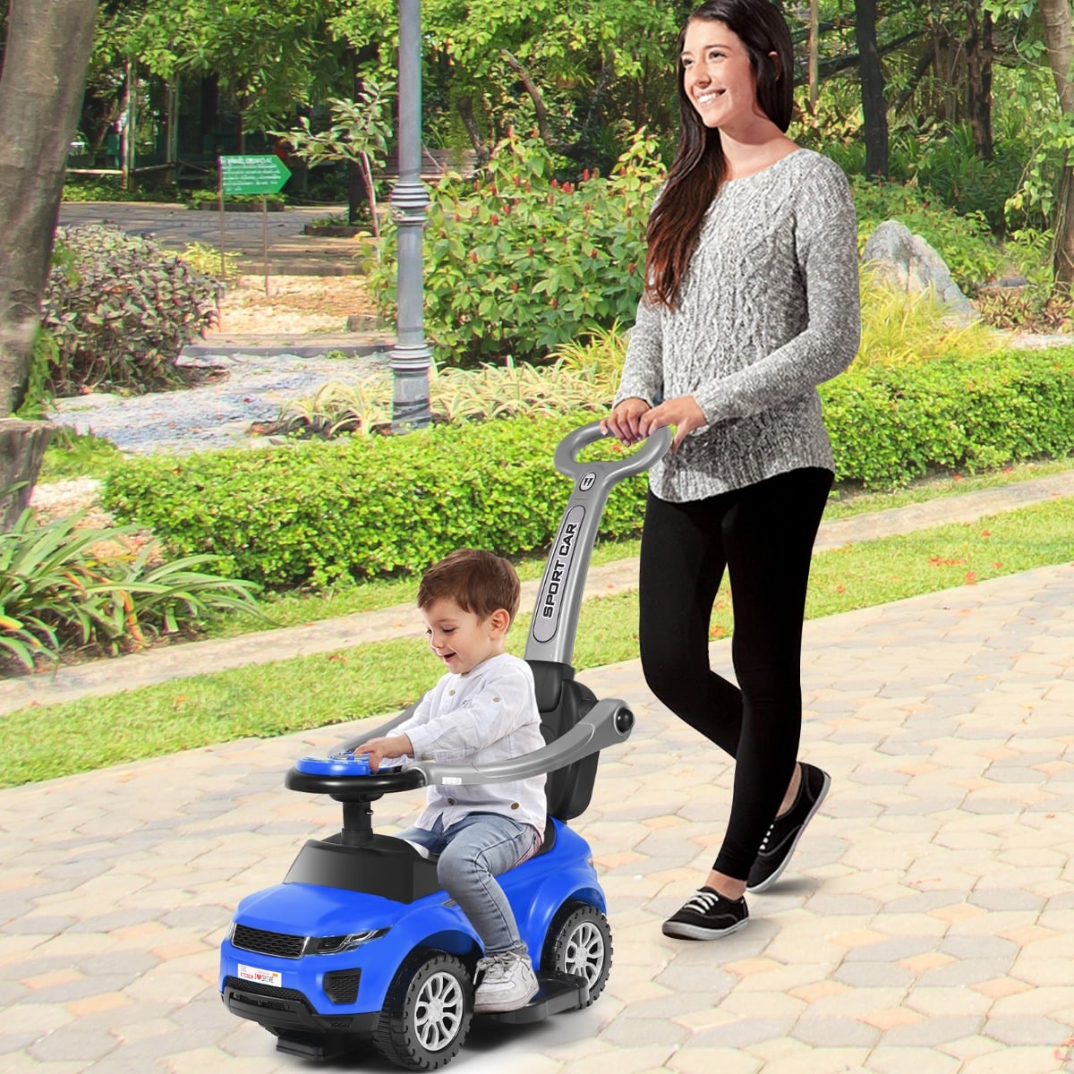 Woman pushing a child on a blue ride on push car stroller in a park