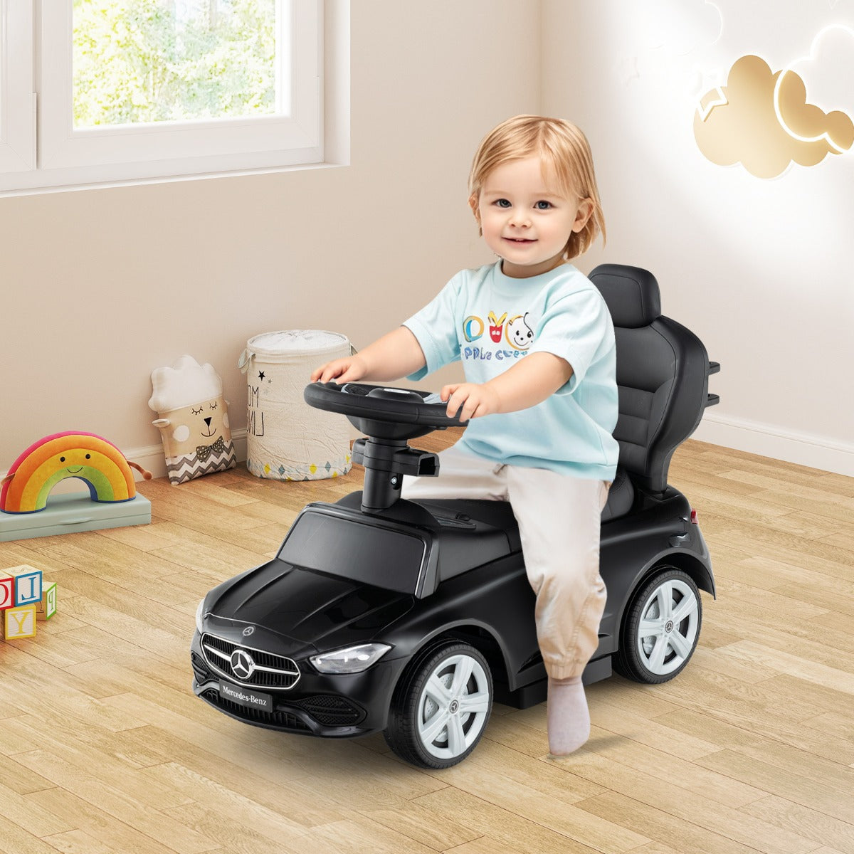 A smiling toddler sits in the black ride on push car, steering it