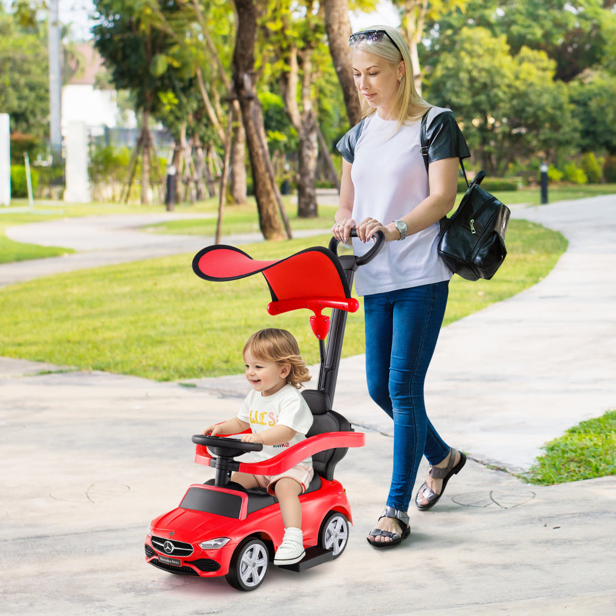 The ride on toy being pushed by an adult along a paved path in a park