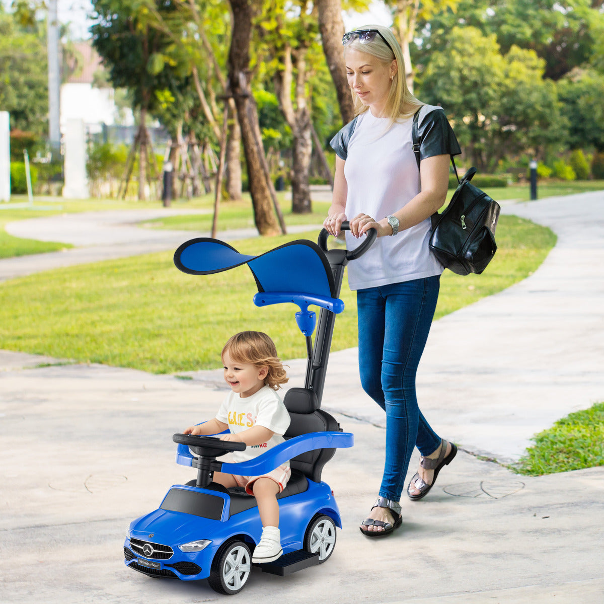 Woman pushing a toddler in the navy blue ride on car in a park