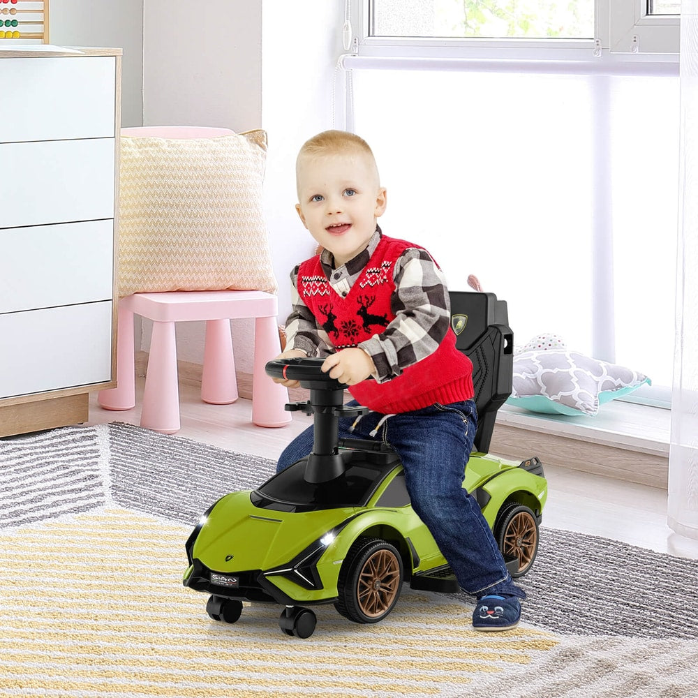 A smiling toddler sits on the green push car, steering it indoors on a rug