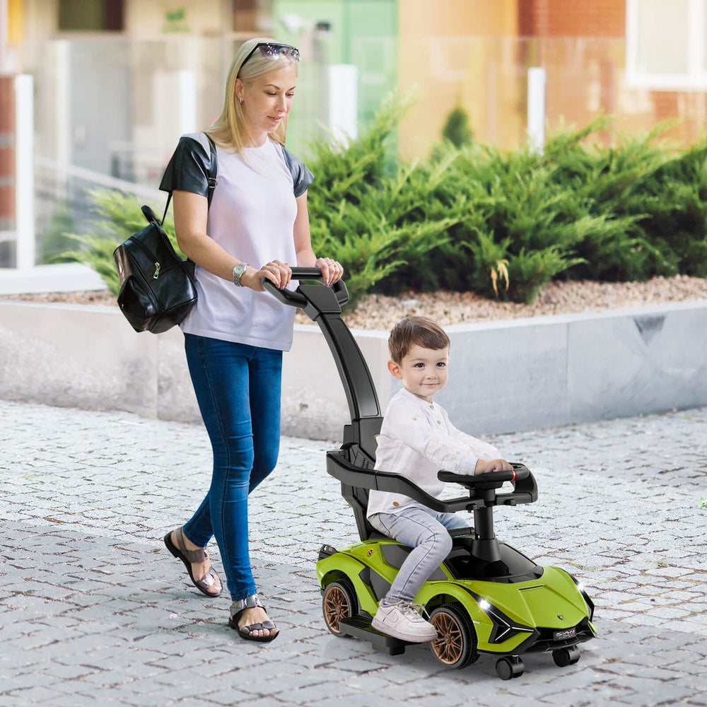 A woman pushes a child on the green ride on car along an outdoor paved path