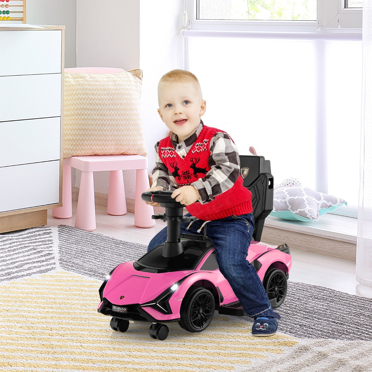 A young boy sits in the pink ride on push car indoors