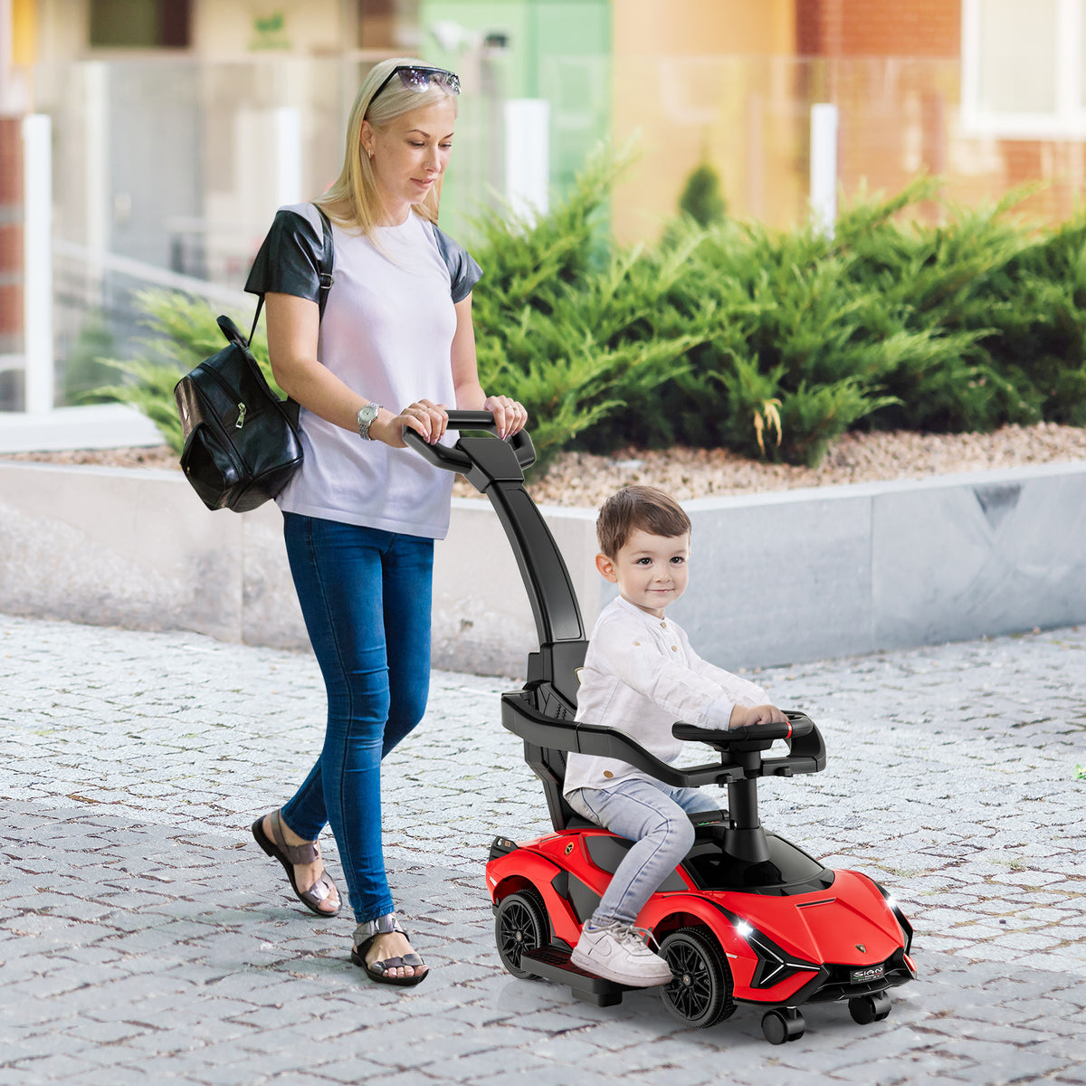 A woman pushing a red ride on push car with a child in it, outdoors