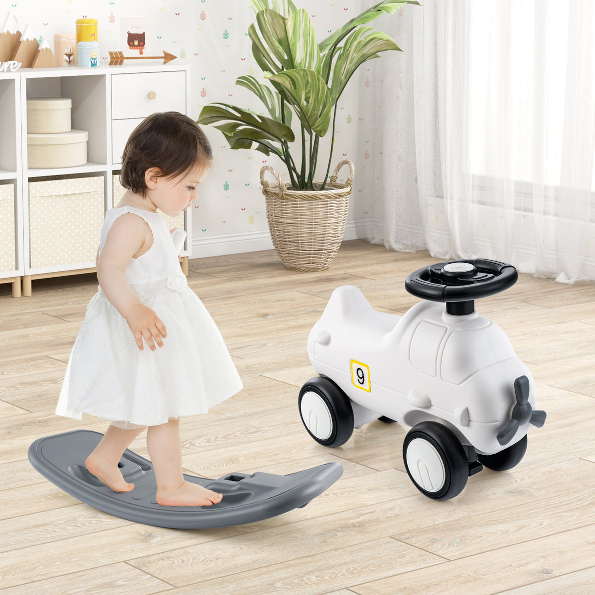 Toddler standing next to the white rocking horse and sliding car on a wooden floor