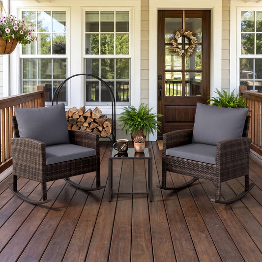 The grey rocking bistro set on a wooden porch with logs and plants