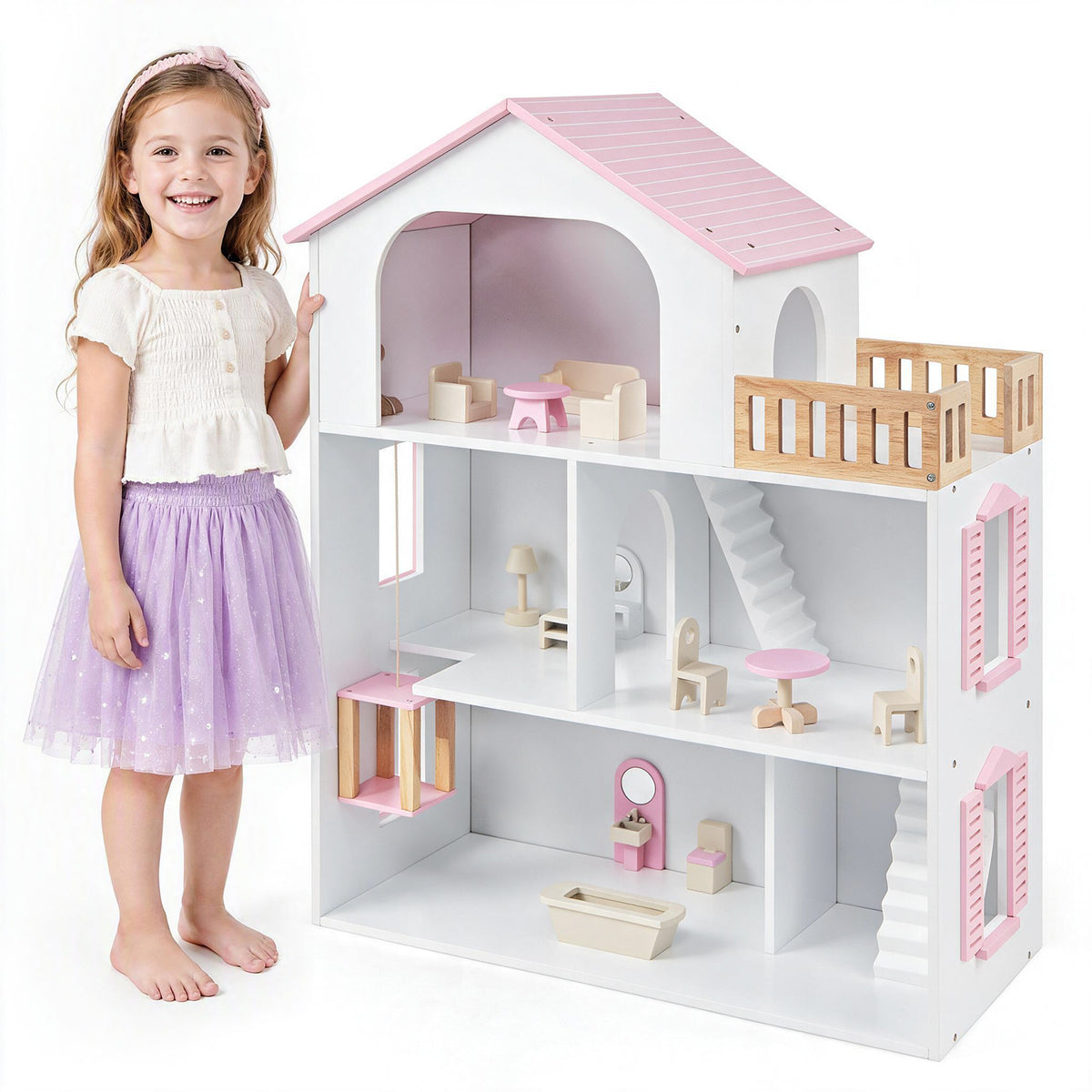 A young girl standing next to the pink wooden dollhouse, smiling at the camera