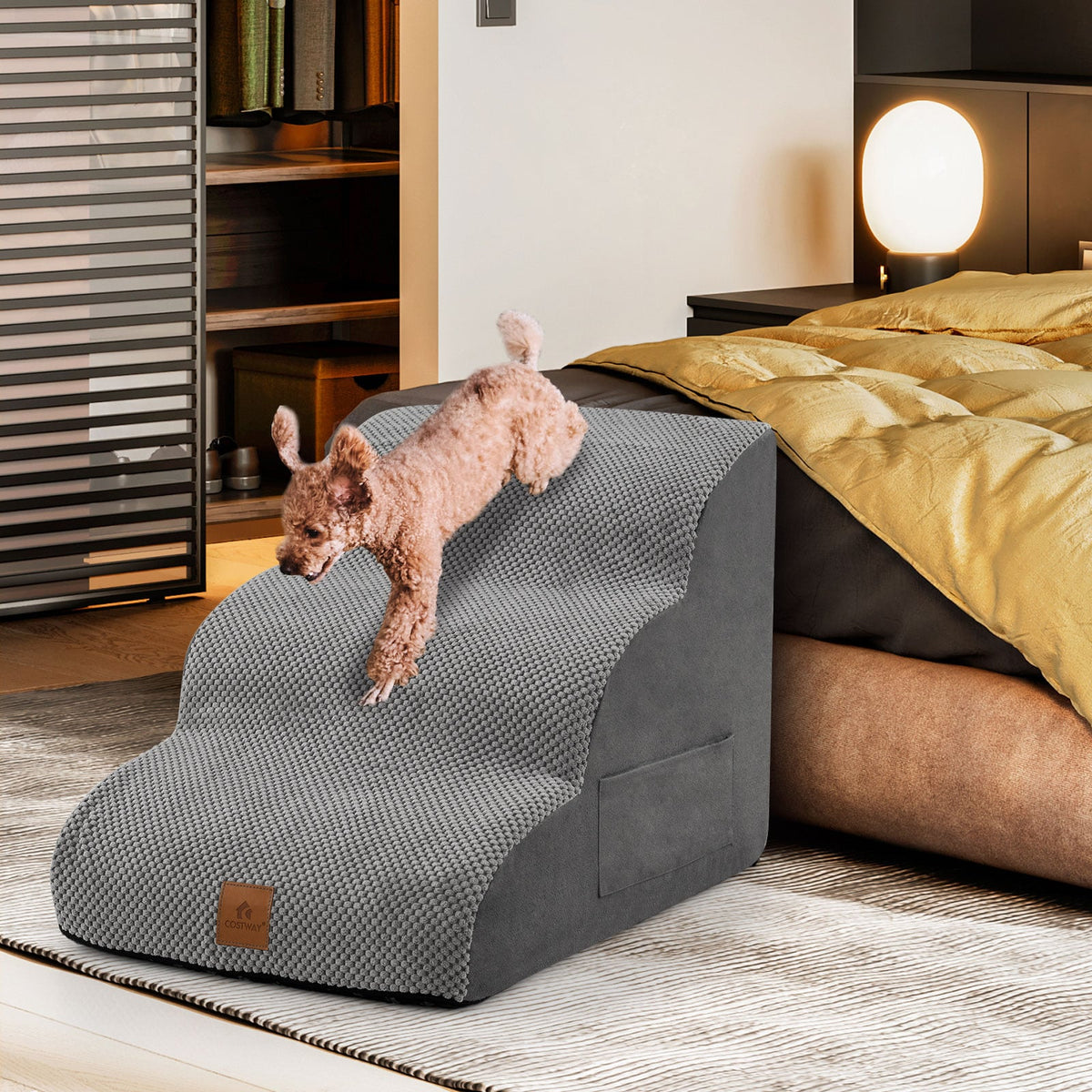 A small dog walks down a grey foam dog ramp next to a bed