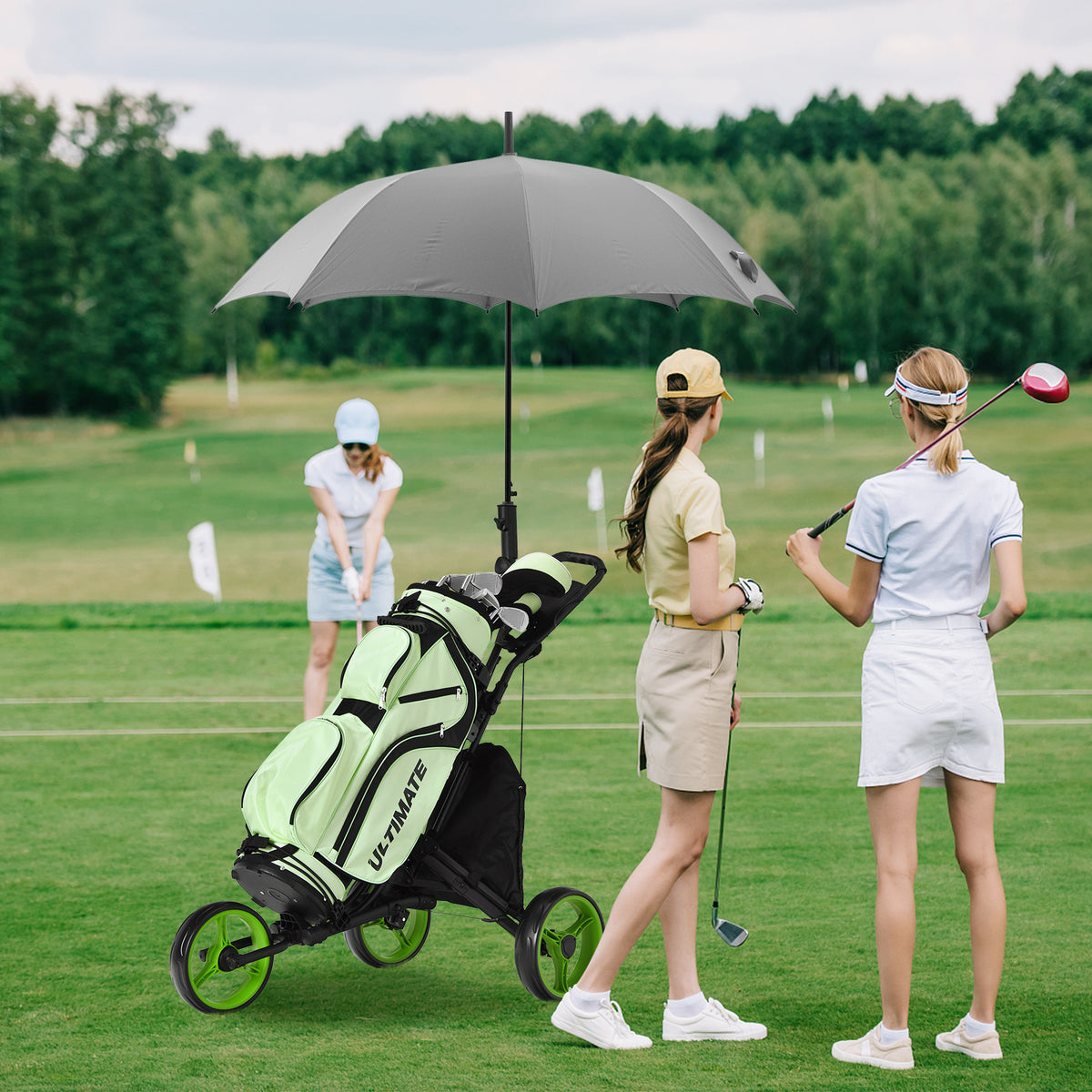 The golf trolley holding a bag with an umbrella on a green course with women playing golf nearby