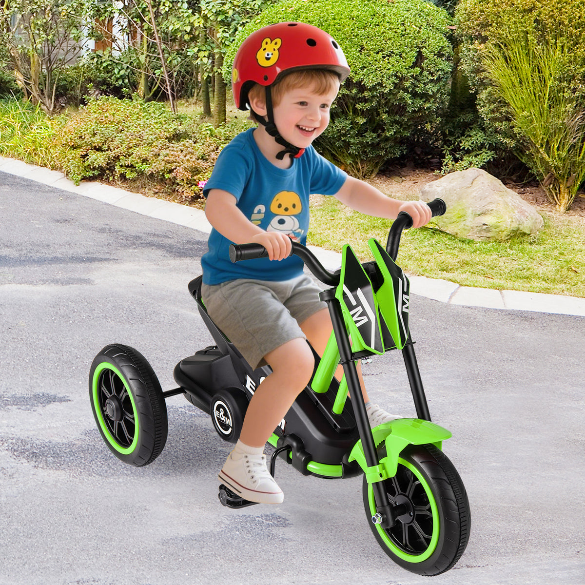 A young boy riding the toddler bike on a paved path in a garden setting