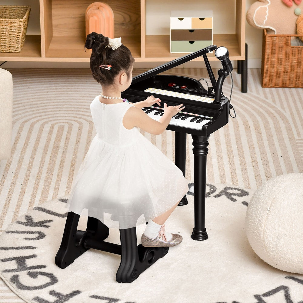 A young girl in a white dress plays the black toy piano with microphone and stool