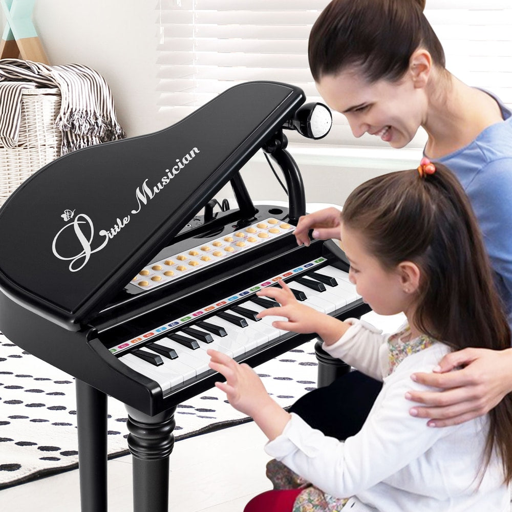 A mother and daughter play the black toy piano together in a room