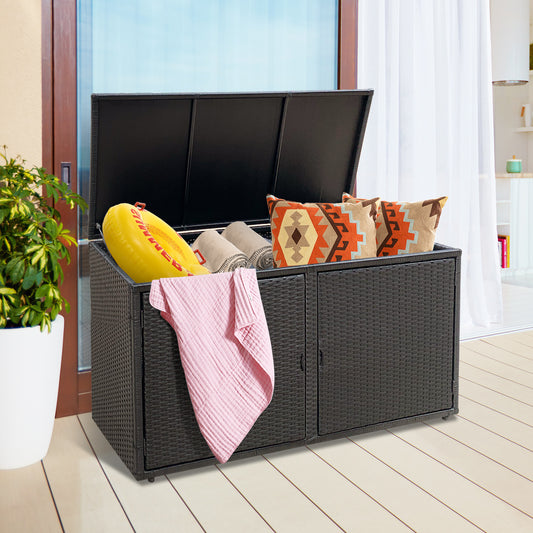 The black outdoor storage box is shown on a patio with its lid open and filled with towels and cushions