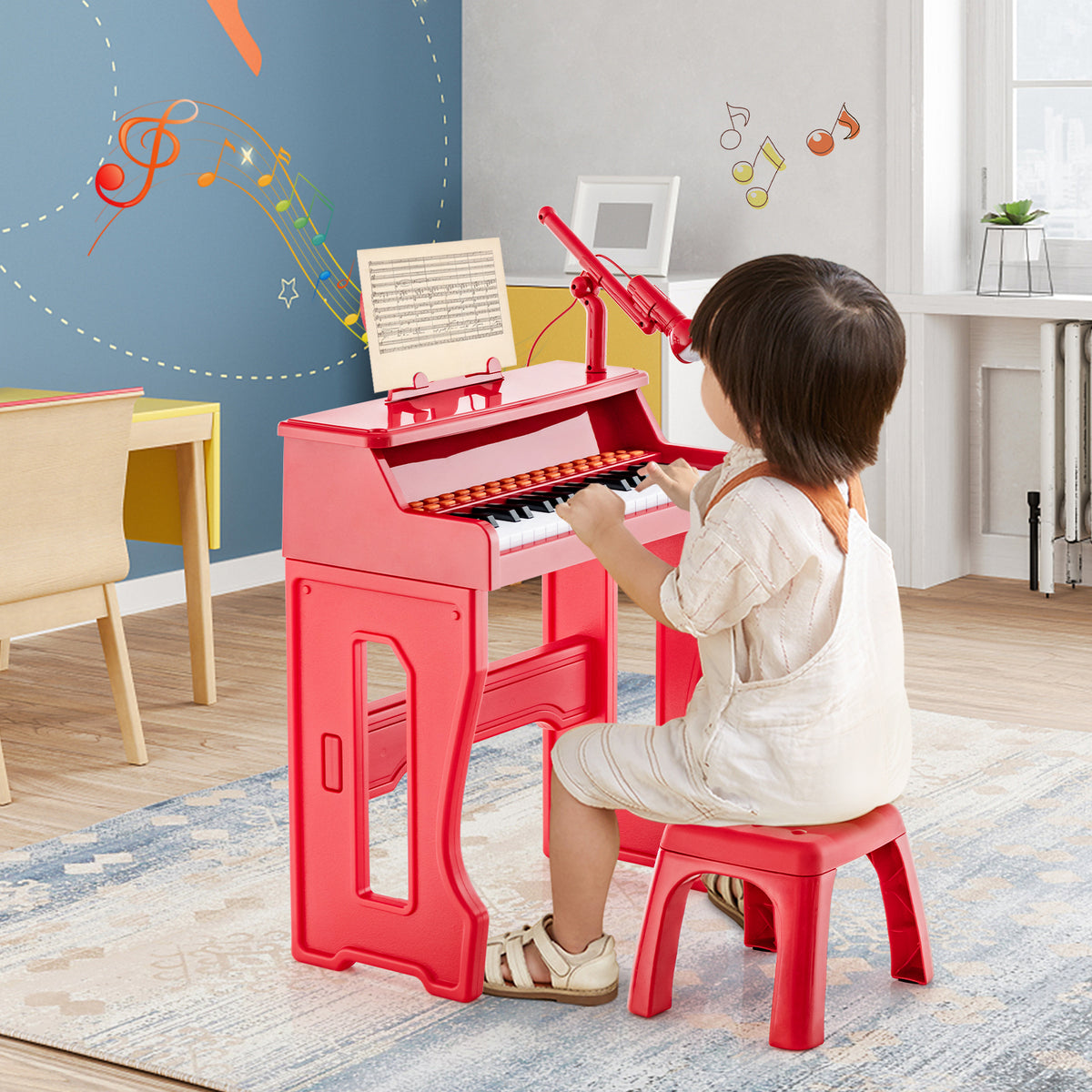 A young child sits at the red electronic piano keyboard playing with the microphone attached